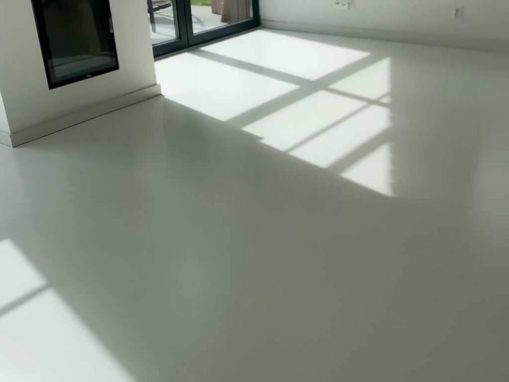 Biały mikrocement w salonie z kominkiem, słońce przez przeszklenia – dom w Koleczkowie
